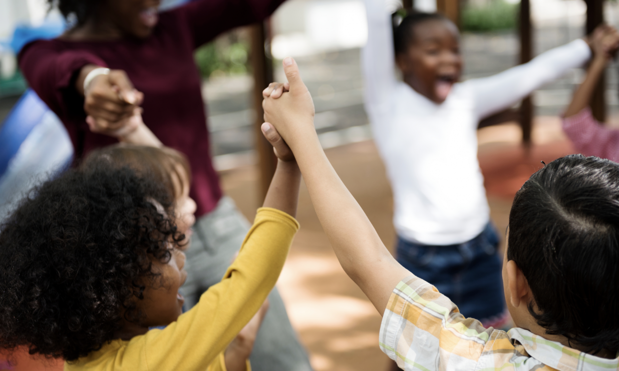 Diverse children and teacher holding hands and playing