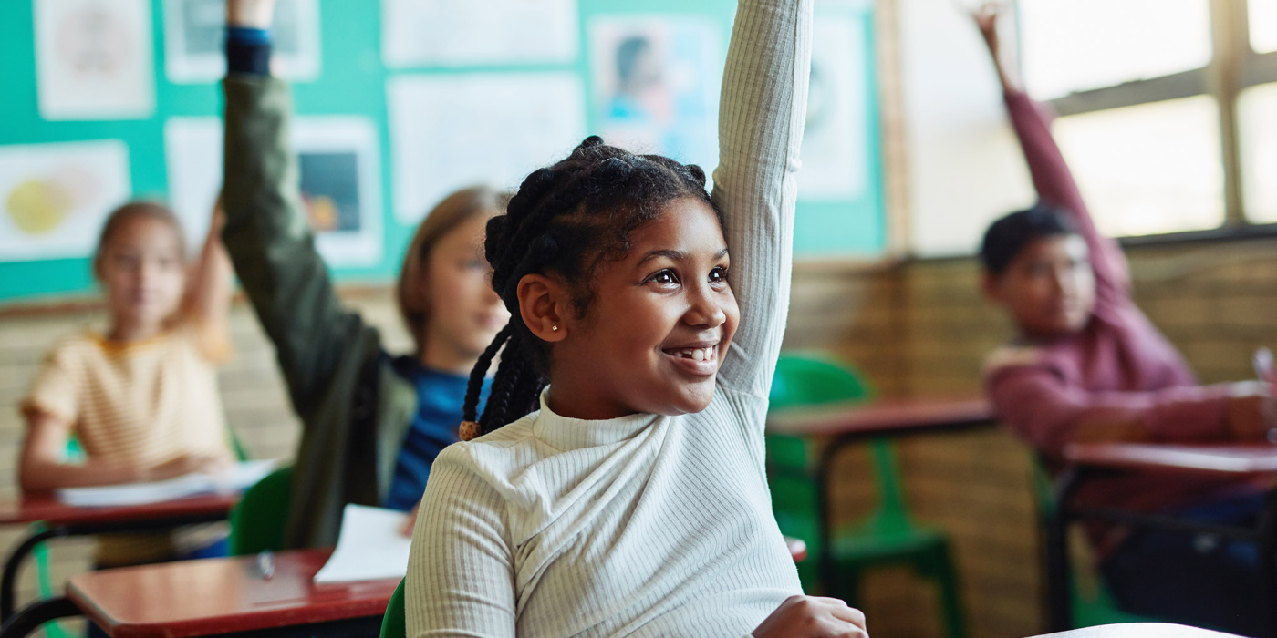 Diverse children raising hands in school