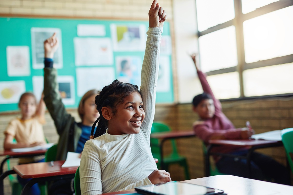 Diverse children raising hands in school