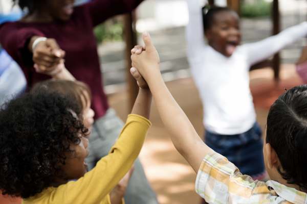 Diverse children and teacher holding hands and playing